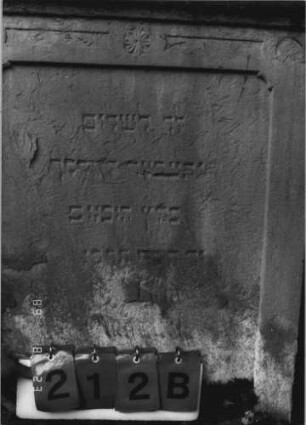 Grabstein 212 (Index: 100110569) Material: Sandstein Zustand: stark verwittert im Giebel mit großem Textverlust, sonst leicht, am unteren Rand stärker verwittert, geringer Textverlust Maße HxBxT: 127x72x17 cm Beschreibung: Stele, Rundbogenabschluß mit Verdachung, Schriftfelder eingetieft Symbolik: 3 Rosetten: Grabstein 212B