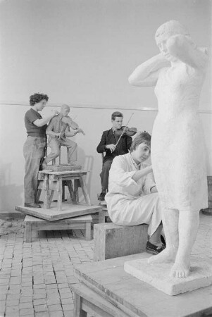 Studenten der Bildhauerklasse von Walter Arnold beim Modellieren. Im Vordergrund die Gips-Statue einerstehenden Frau, ein Kopftuch bindend (1960/1962)