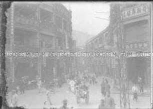 Belebte Geschäftsstraße mit zahlreichen Passanten und Rikschafahrern in Macau, China