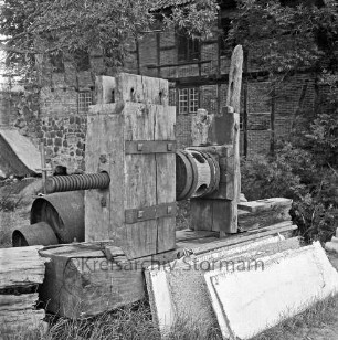 Drahtmühle: Restaurierung: vorn Mühlenwerk der Papiermühle mit Holzbohlen: dahinter Bäume: rechts Stapel mit Brettern: dahinter Baum und Äste