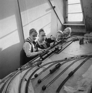Eisenbahner in Uniform mit drei Kindern an einer Modellbahnanlage (Serie Deutsche Reichsbahn - Brigade "Otto Buchwitz")