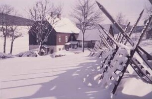 Blick auf ein Haus im Erzgebirge im Winter mit Schneezäunen im Vordergrund