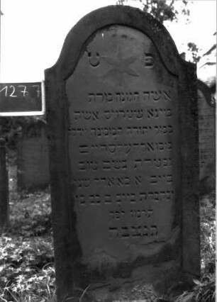 Grabstein 1277 (Index: 100104517) Material: Sandstein Zustand: oben und unten verwittert (Abblätterungen) Maße HxBxT: 170x75x17 cm Beschreibung: Stele mit eingezogenem Rundbogenabschluss, Schriftfeld eingetieft mit Konvexbogenabschluss, im Bogenfeld Blüte Symbolik: Blüte: Grabstein 1277