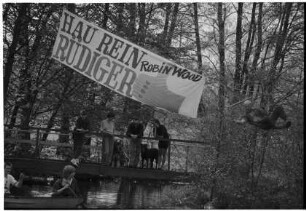 Mühlenteich: bei Steg, zwischen Bäumen: Begrüßungstransparent der Umweltorganisation Robin Wood "Hau rein, Rüdiger!": Organisationsmitglieder auf Steg, in Paddelboot: in Hängematte Umweltaktivist Rüdiger Nehberg