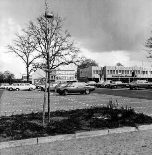 Markt: vorn Parkplatz mit Pkws: dahinter Einkaufszentrum mit Filiale der Kreissparkasse Stormarn: links Bäume