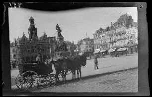 Saint-Quentin (Dep. Aisne, Frankreich): Zweispänner mit Kutsche, dahinter der Stadtplatz mit Denkmal [für die Verteidigung von St. Quentin (1557)], im Hintergrund das Rathaus mit Glocken- und Uhrturm
