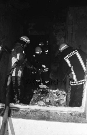 Brand: Einfamilienhaus: Blick durch Fenster in Zimmer: Feuerwehrmänner mit Feuerwehrschlauch und Schaufel beim Löschen von Brandnestern: 2. Juni 1999