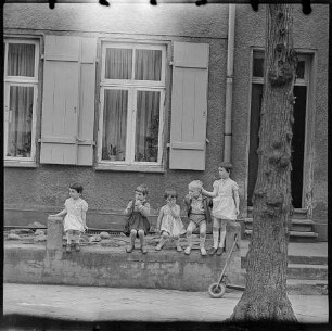 Fünf Kinder sitzen vor einem Wohnhaus, 1960er Jahre. SW-Foto © Kurt Schwarz.