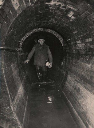 Unter den Straßen von Berlin. Mann im Abwasserkanal mit Taschenlampe