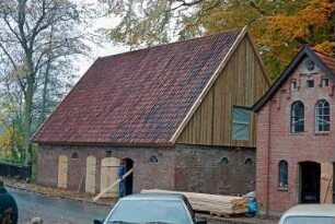Nütschau: Schloßstraße 44: gegenüber von ehemaliger Kornwassermühle: links Pferdestall, rechts Backhaus [angeschnitten]: Restaurierung: Erneuerung von Türen, Verbretterung an Giebel: Stapel mit Holzbrettern, Arbeiter