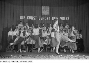 Tanzende Paare, im Hintergrund Chor und Orchester beim Kreisausscheid für Volkskunst