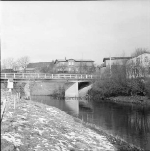 Trave: vorn Böschung: hinten links Brücke: am rechten Ufer Sträucher und Bäume: dahinter Bauernhäuser: Winter