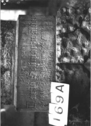 Grabstein 169 (Index: 99899021) Material: Sandstein Zustand: stark verwittert Maße HxBxT: 140x54x25 cm Beschreibung: aufgesockelte Stele mit Konvexbogenabschluss, eingeritzte Mittelpalmette und Voluten, unterer Sockel felsartig gearbeitet Symbolik: Palmette, Voluten: Grabstein 169A