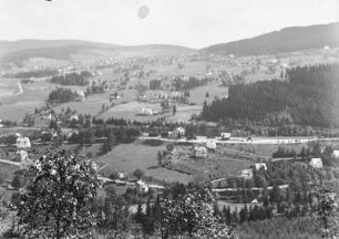 Nové Hamry : Blick vom westlichen Hang des Rohlautals über Nové Hamry mit dem Bahnhof in der Bildmitte, der Kirche am linken Bildrand und dem oberen Ortsteil im Hintergrund.