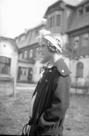 Portrait einer jungen Frau im Profil nach links, vor einer Bergwirtschaft stehend