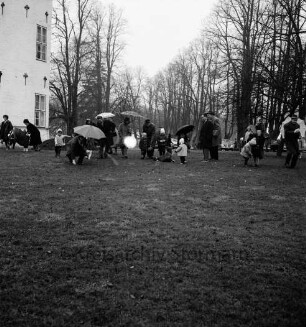 Schlosspark: Ostereiersuchen: Kinder suchen im Regen: Erwachsene mit Regenschirmen: links Schloss