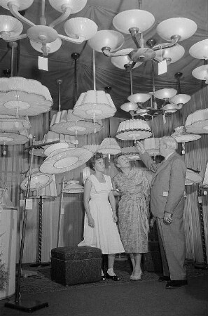 Drei Personen begutachten auf der Leipziger Herbstmesse 1955 ausgestellte Deckenlampen