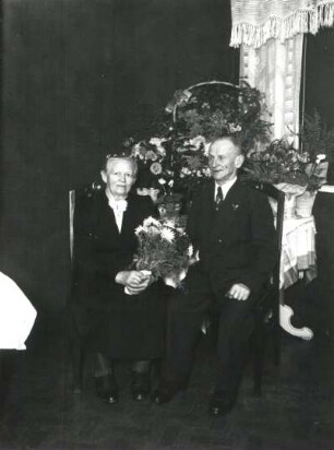 Goldenes Hochzeitspaar vor Tisch mit Blumen sitzend