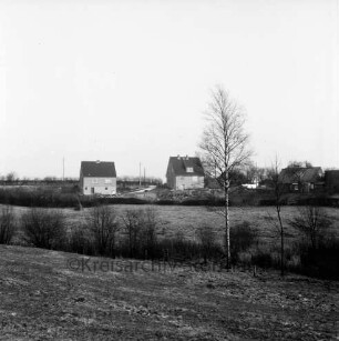 Neubausiedlung: zwei Einfamilienhäuser: davor Knicklandschaft mit Geländeeinschnitten