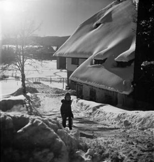 Kind vor tief verschneitem Haus