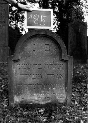 Grabstein 185 (Index: 100111376) Material: Sandstein Zustand: gut Maße HxBxT: 71x60x8 cm Beschreibung: Stele, schräg eingezogener Rundbogenabschluß, Schriftfeld eingetieft: Grabstein 185