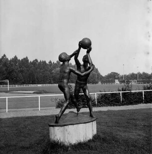 Sporteinrichtungen: Sportplatz: vorn auf Rasen Kunst im öffentlichen Raum: Bronzeskulptur mit zwei ballspielenden Jungen