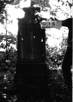 Grabstein 16 (Index: 100101164) Material: Sandstein mit schwarzer Granitplatte unten Zustand: gut Maße HxBxT: 154x51x22 cm Beschreibung: Stele, getreppter Sockel, getreppter Abschluß mit Kugelaufsatz, Schriftfeld mit Maßwerk Symbolik: Maßwerk: Grabstein 16