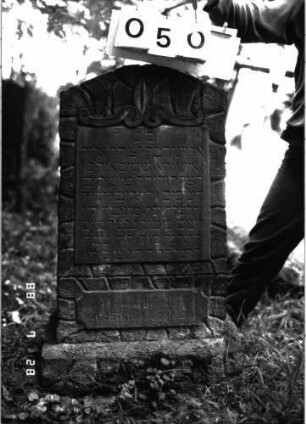 Grabstein 50 (Index: 100101232) Material: Sandstein Zustand: leicht verwittert Maße HxBxT: 96x46x22 cm Beschreibung: rusticaartige Stele, Sockel, Segmentbogenabschluß, Schriftplatten rechteckig Symbolik: Volutenband als oberer Schriftfeldrand: Grabstein 50