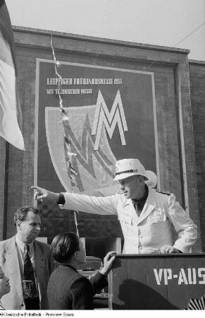 Besucher der Leipziger Messe 1954 an einem Informationsstand der Volkspolizei, im Hintergrund Werbung für die Leipziger Frühjahrsmesse 1955