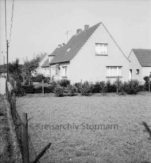 Neubausiedlung: vorn Wiese mit Zaun: dahinter Einfamilienhäuser mit Gärten