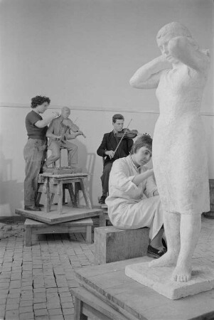 Studenten der Bildhauerklasse von Walter Arnold beim Modellieren. Im Vordergrund die Gips-Statue einerstehenden Frau, ein Kopftuch bindend (1960/1962)