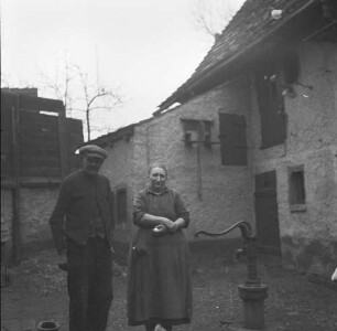 Familienbilder : Altes Paar neben einer Schwengelpumpe, wohl im Hof eines kleines Gehöfts