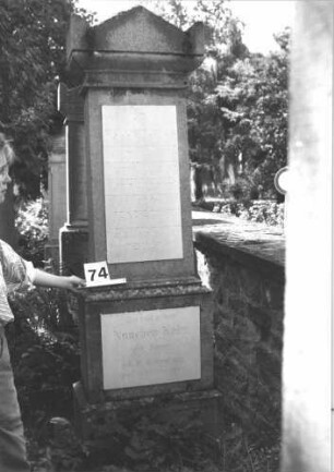 Grabstein 74 (Index: 100114195) Material: Kalkstein mit zwei weißen Marmorplatten Zustand: gut Maße HxBxT: 210x66x38 cm Beschreibung: Stele, getreppter Sockel, Giebel mit Eckakroteren, Schrifttafel rechteckig: Grabstein 74