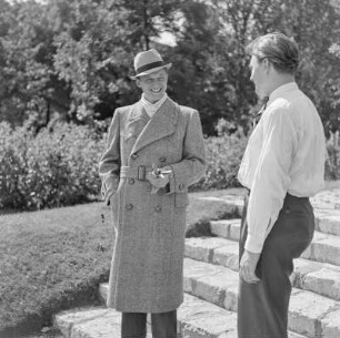 Mann in Hut und Mantel im Park vor einem Denkmal