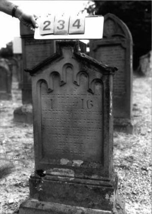 Grabstein 234 (Index: 99797715) Material: Sandstein, weiß Zustand: stark verwittert Maße HxBxT: 107x60x20 cm Beschreibung: Stele, Giebel rechteckig erhöht, profilierter Sockel Symbolik: Rundbogenfries: Grabstein 234