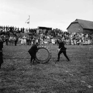 Tremsbüttel: Amtsfeuerwehrfest: Festplatz: Übungen: Rollen eines großen Ackerschlepperreifens über Hindernisparcour durch zwei Feuerwehrmänner: im Hintergrund Zuschauer