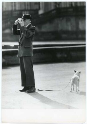 Mann im Anzug mit Hut, Brille und Hund beim Fotografieren