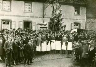 Gruppenbild vieler Personen zur Kirchweihe, vor einem Haus am Straßenrand stehend, mit geschmücktem Baum. Bundenthal