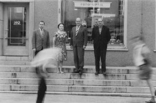 Niesky. Mehrere Personen (Lehrer oder Dozenten ?) auf den Stufen vor einem HO-Industriewarenladen "Foto - Optik"