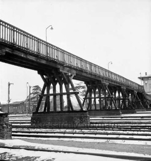 Bahnhofsgelände: Holzbrücke für Fußgänger, über westliche Gleisanlagen: hinten Bahnhofsinsel, darauf rechts Bahnhofsgebäude [angeschnitten], links Güterbahnhof, Signal: Lichtmasten: im Winter