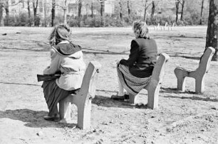 Berlin. Zwei junge Frauen sitzen auf Banksockeln (Serie "Berliner Schnappschüsse"). Rückansicht
