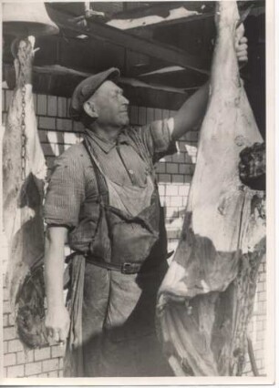 In einer Fleischwarenfabrik. Ein Schlachter hängt im Schlachthaus Schweinehälften auf