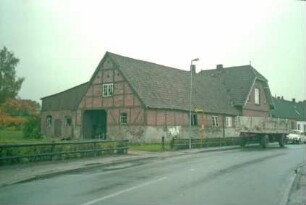 Bauernhaus: traufständiges Fachwerkgebäude: Giebel Wirtschaftstrakt mit Scheunentor: links Stallanbau: rechts Querbau Wohntrakt mit Giebel zur Straße: davor Bushaltestelle