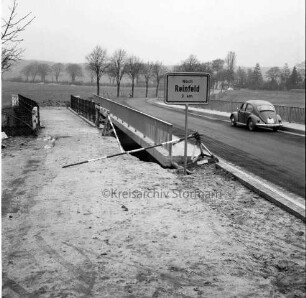 Trave: Brückenneubau: Spannbetonbrücke nach Fertigstellung: links alte Holzbrücke: im Vordergrund Straßenschild Richtung Reinfeld und VW-Käfer: hinten Bäume