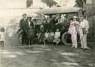 Manila (Philippinen), Hafen. Touristen der Hapag, an und in einem Automobil mit einheimischem Fahrer und Kindern vor traditionellen Wohnhäusern posierend