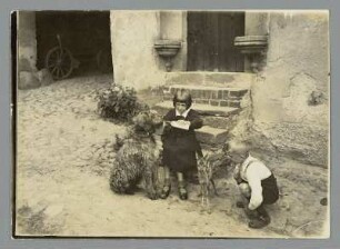 Sachsen. Zwei Kinder mit Hund und Rehkitz im Hof eines Gehöftes