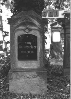 Grabstein 111 (Index: 99788808) Material: Sandstein und schwarze Glasplatte Zustand: sehr stark verwittert mit vollständigem Textverlust, später aufgesetzte Glasplatte, zerbrochen und repariert, Aufsatz fehlt Maße HxBxT: 137x61x15 cm Besonderheit: Schrift vergoldet: Grabstein 111