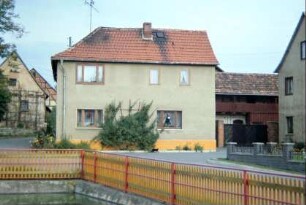 Bauernhaus am Dorfplatz mit Laubenganghaus; vorn Dorfteich mit Zaun
