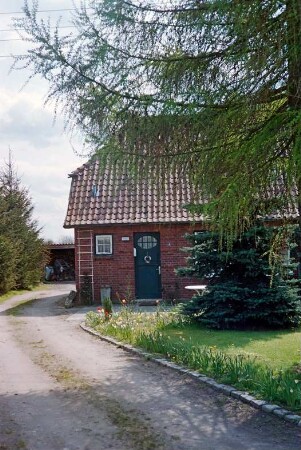 Blumendorf 4: traufständige Doppelkate aus Backstein: Straßenfront, Teilansicht links: Eingangstür, Hausnummer, Rankgitter: vorne Vorgarten: links Einfahrt, hinten Schuppen