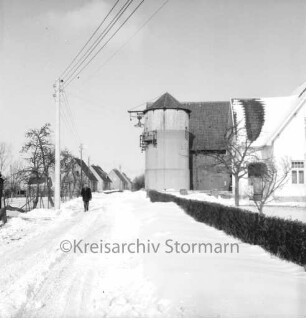 Rethwischdorf: Neubausiedlung: links davor Strommast: daneben Mann: rechts Bauerngehöft mit Silo: vorn rechts Hecke: Winter